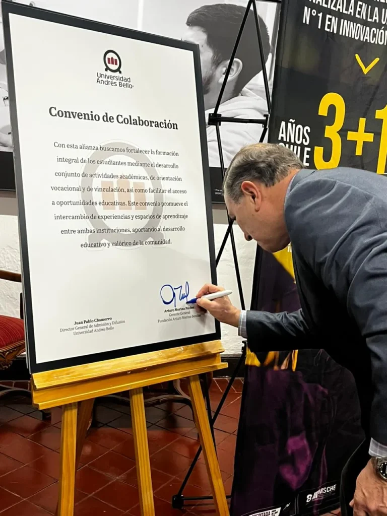 Man signs a framed document titled 'Convenio de Colaboración' on a wooden easel at an event, with the Universidad Andrés Bello logo visible.