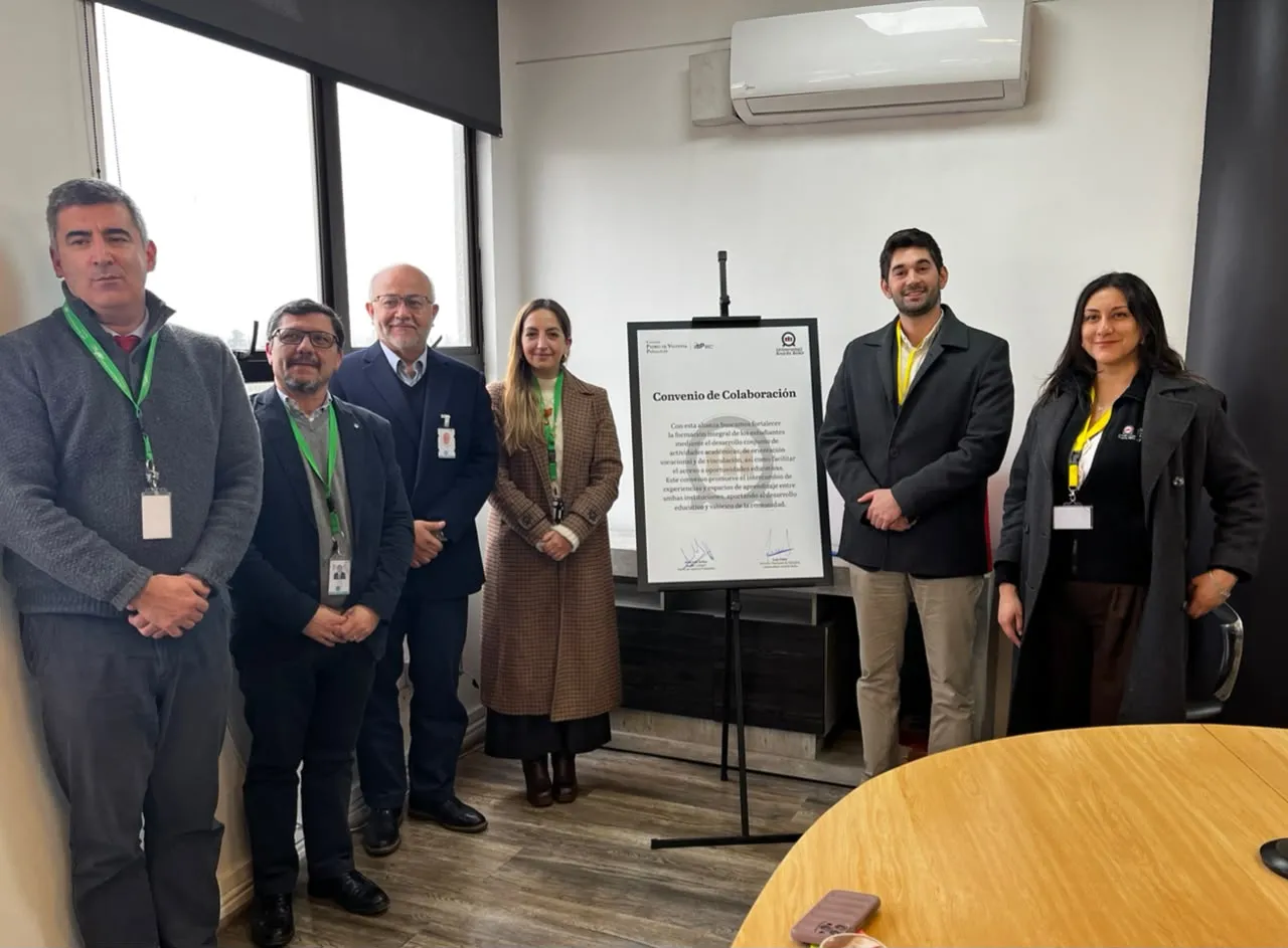 Six professionals in business attire pose in a conference room beside a framed 'Convenio de Colaboración' poster on a stand.