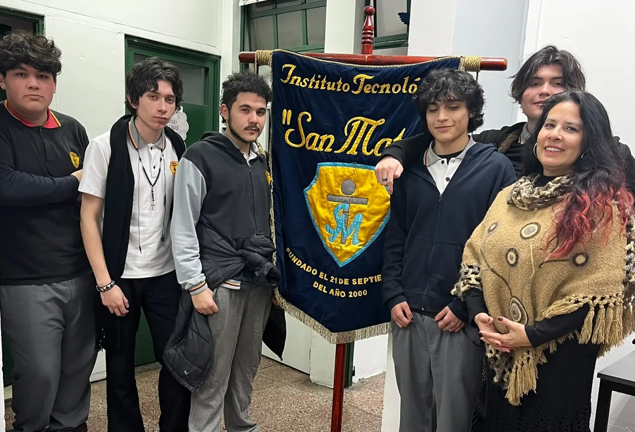 Six students and a teacher pose with a blue school banner in a hallway.